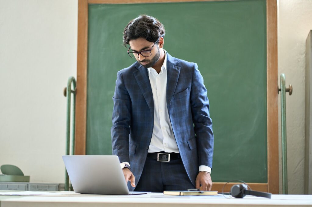 Young indian business man working on laptop computer standing in office.